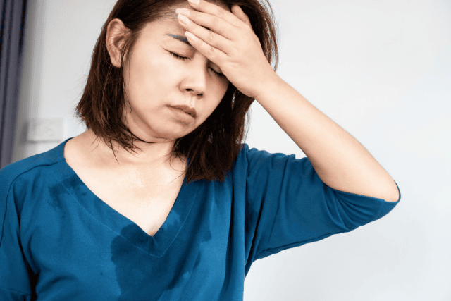 汗をかき、額に手を当てている女性