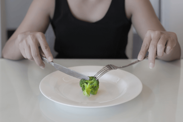 さらに乗った一つのブロッコリーをナイフとフォークで食べようとしている人